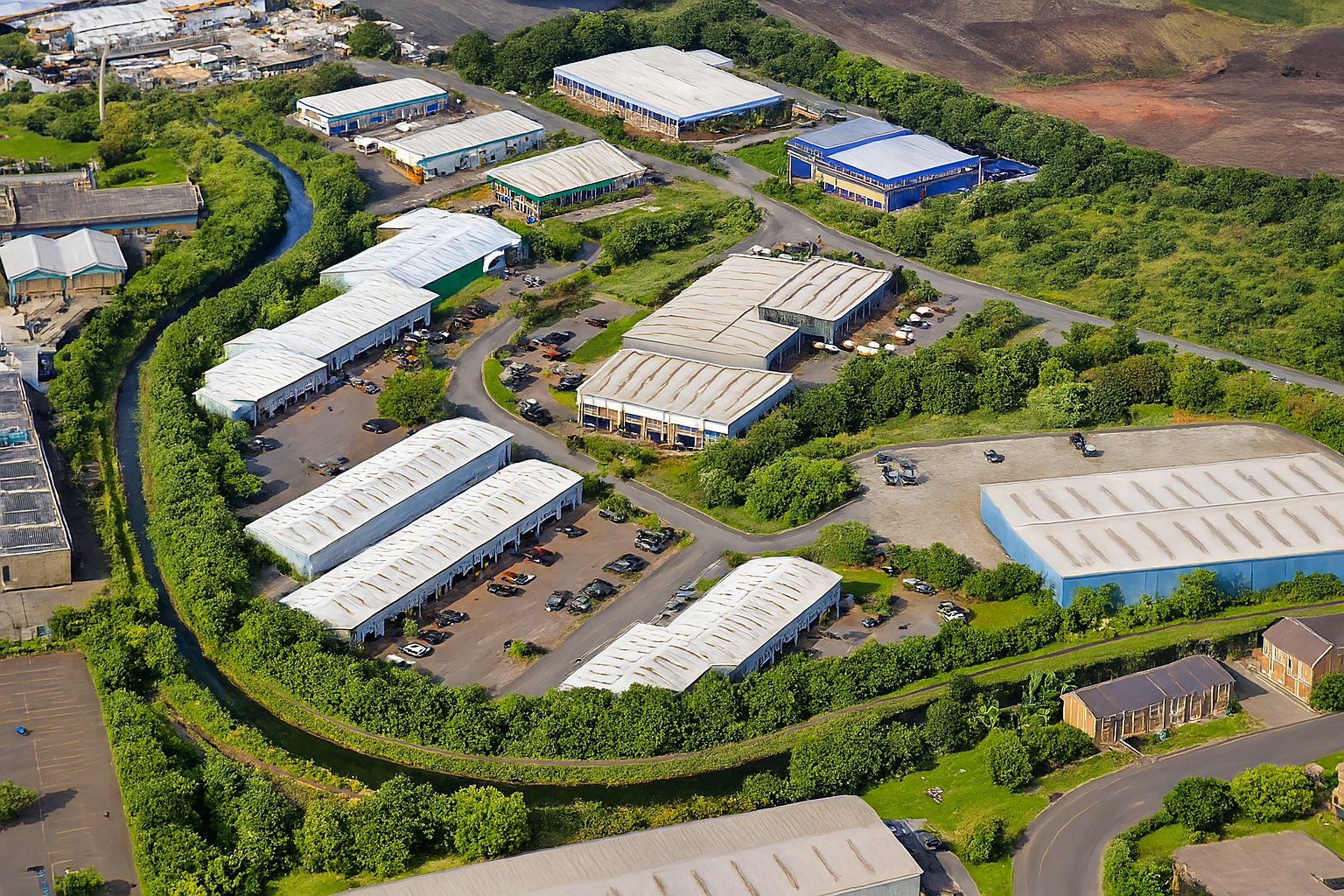 Aerial view of a modern industrial estate with white warehouse buildings, parking lots, surrounding greenery, and a winding waterway in Ghana